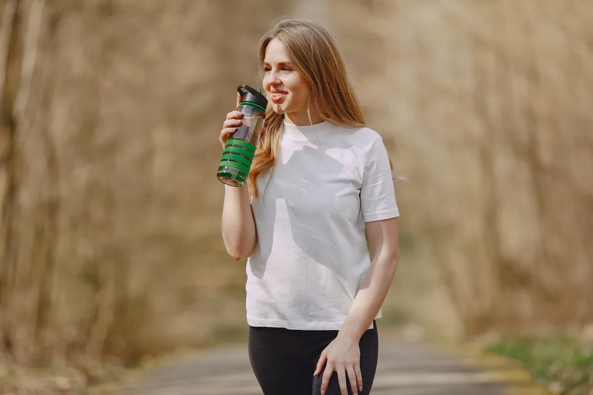 Žena venku drží lahev se zeleným nápojem