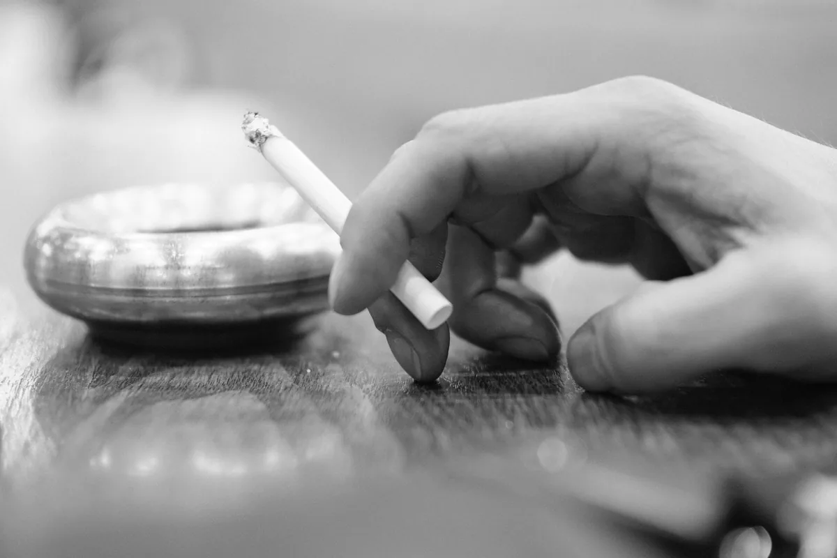 Ruka s cigaretou vedle popelníku